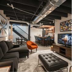 Modern basement living area with a sectional sofa, orange chair, TV, and bar with stools in the background. Chic Basement Ideas, Low Ceiling Basement Ideas, Basement Vibes, Ceiling Basement Ideas, Chic Basement, Basement Unfinished, Unfinished Basements, Low Ceiling Basement, Ceiling Basement