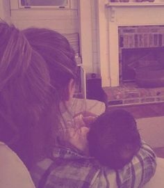 a woman holding a baby in her arms while sitting on a couch next to a fire place