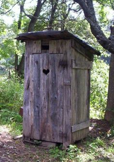 a wooden outhouse in the woods surrounded by trees