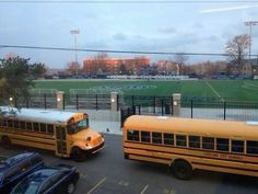 two yellow school buses parked in front of a soccer field