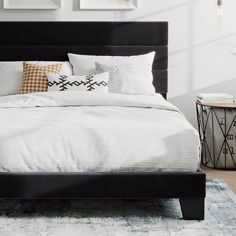 a bed with white sheets and black headboard in front of pictures on the wall