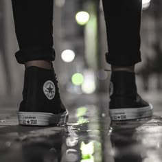 a person's feet in black and white sneakers on a wet floor with lights behind them