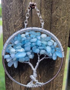 a wire wrapped tree of life hanging from a wooden fence with blue glass beads on it