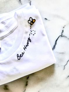 a white t - shirt with a bee embroidered on it