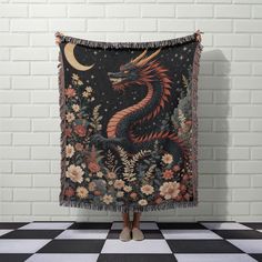 a woman standing in front of a brick wall holding up a tapestry with a dragon on it