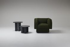 two black tables and a green chair in front of a white wall with grey background