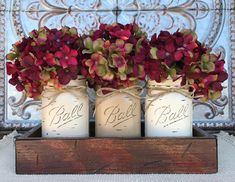 three mason jars with flowers in them are sitting on a wooden box that says ball