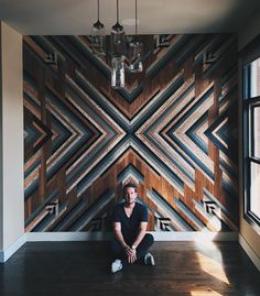 a man sitting on the floor in front of a wooden wall with geometric designs and lights