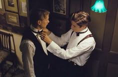 two men are fixing their ties in a room with pictures on the wall and green light above them