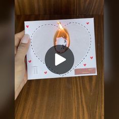 someone is holding up a card with a burning candle in the shape of a heart