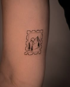 a small tattoo on the arm of a person with mountains and trees in the background