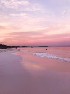 people walking on the beach at sunset with pink clouds in the sky and some water