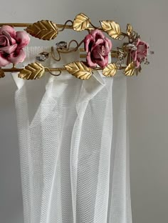 pink flowers are hanging from a gold metal curtain rod in front of white sheer curtains