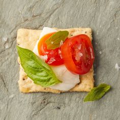 a cracker with cheese, tomato and basil on it sitting on a stone surface