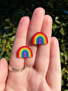 two rainbow earrings are sitting on someone's hand in front of some bushes and trees