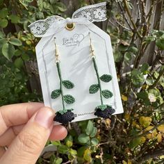 a person holding up a pair of earrings with green leaves on the front and black flowers on the back