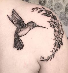 a hummingbird flying through the air with flowers around it's neck and wings