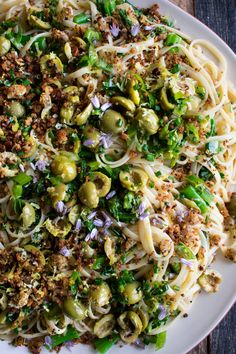 a white plate topped with pasta covered in olives and other toppings on top of a wooden table