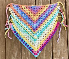 a multicolored crocheted triangle with tassels on top sitting on a wooden surface