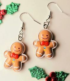 two gingerbread cookies are hanging from silver earwires on a white surface with holly decorations