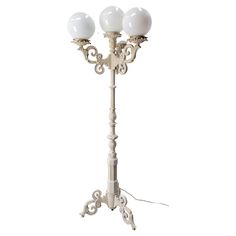 a white floor lamp with three lights on each side and an ornate design around the base