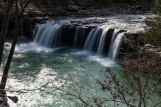 a small waterfall in the middle of a forest filled with trees and water flowing down it's sides