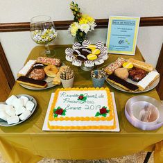 a table topped with cakes and desserts on top of a yellow cloth covered table