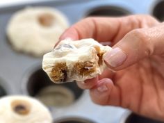 a hand holding a half eaten doughnut in front of muffin tins