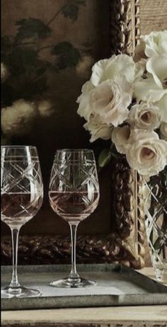 two wine glasses sitting on a tray next to a vase with white flowers in it