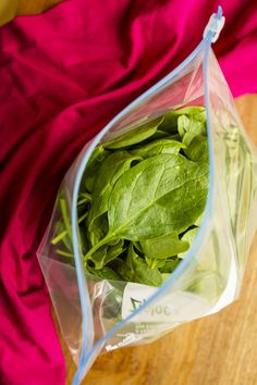 a plastic bag filled with spinach leaves on top of a wooden table next to a pink cloth