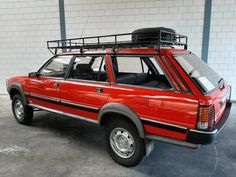 a red car parked in a garage next to a white brick wall with a luggage rack on the roof