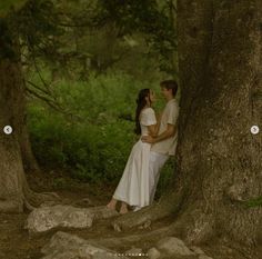 a man and woman standing next to each other under a tree in the middle of a forest