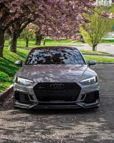 the front end of a gray car parked in a parking lot next to some trees