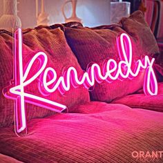 a pink neon sign that says brandy on top of a bed with pillows and blankets