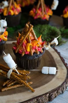 cupcakes with marshmallows and candy sticks on a wooden tray decorated with autumn leaves