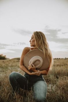 a woman sitting in the middle of a field with a hat on her head and looking off into the distance