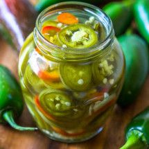 a jar filled with pickles sitting on top of a wooden table next to green peppers