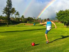 a man kicking a soccer ball on top of a lush green field next to a rainbow