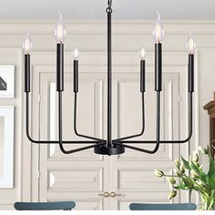 a black chandelier with six candles hanging from it's center and four chairs in the back