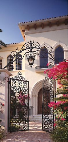 an open gate leading to a house with pink flowers on the front and side doors