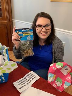 a woman sitting at a table holding up a bag of gifts and giving the thumbs up sign