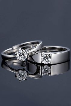 two white gold wedding rings with diamonds on the top and bottom, against a dark background