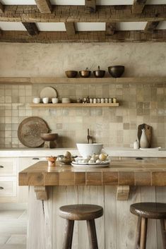 a kitchen with two wooden stools next to a counter and shelves filled with dishes