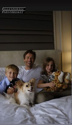 a man, two children and a dog sitting on a bed