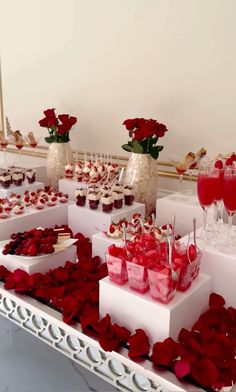 a table topped with lots of desserts and cups filled with red flowers on top of it