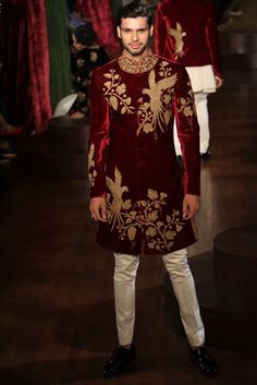 a man in a red and gold outfit standing on a wooden floor with other people