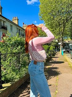 a woman with red hair is standing on the sidewalk and drinking from a water bottle