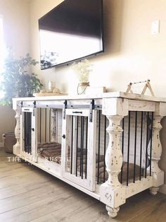 a white dog crate sitting on top of a hard wood floor next to a tv