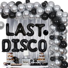 a table topped with black and silver balloons next to a sign that says last disco