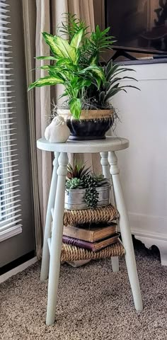 a small white table with some plants on top of it and a window in the background